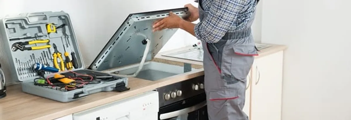 Cooktop repair technician lifting a built-in stovetop for service in Columbus, GA